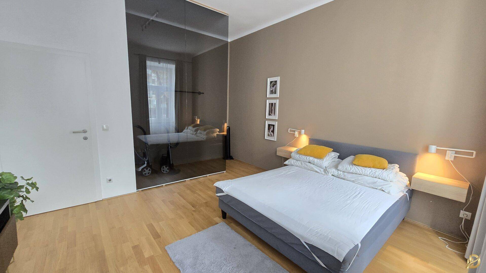 Schlafzimmer mit großem Spiegelkleiderschrank, Holzboden und gemütlichem Doppelbett.