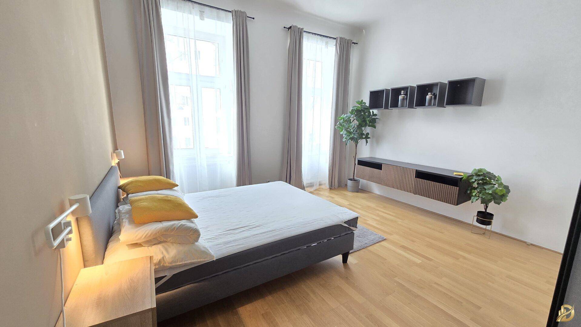 Helles Schlafzimmer mit Holzboden, zwei Fenstern und moderner Einrichtung.