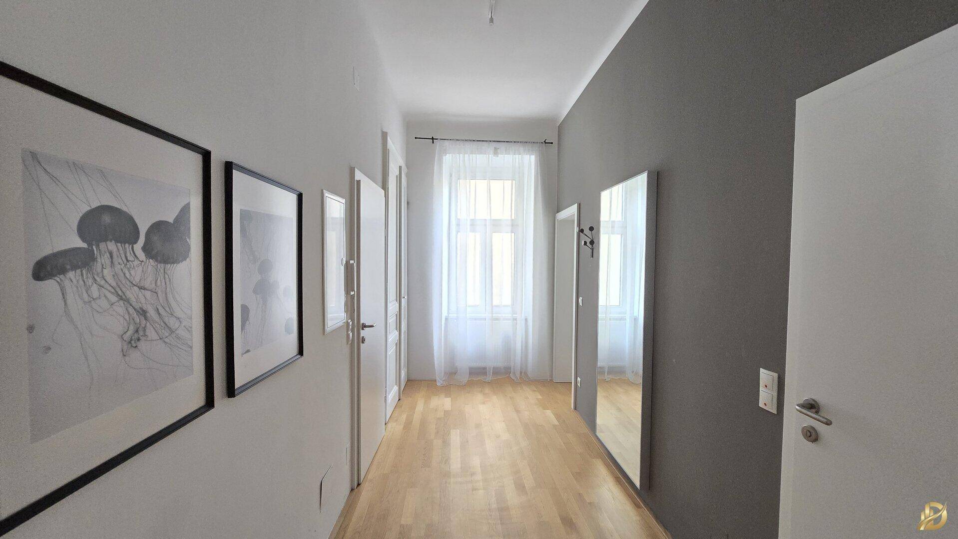 Geräumiger Flur mit Holzboden, Spiegel und Fenster für natürlichen Lichteinfall.