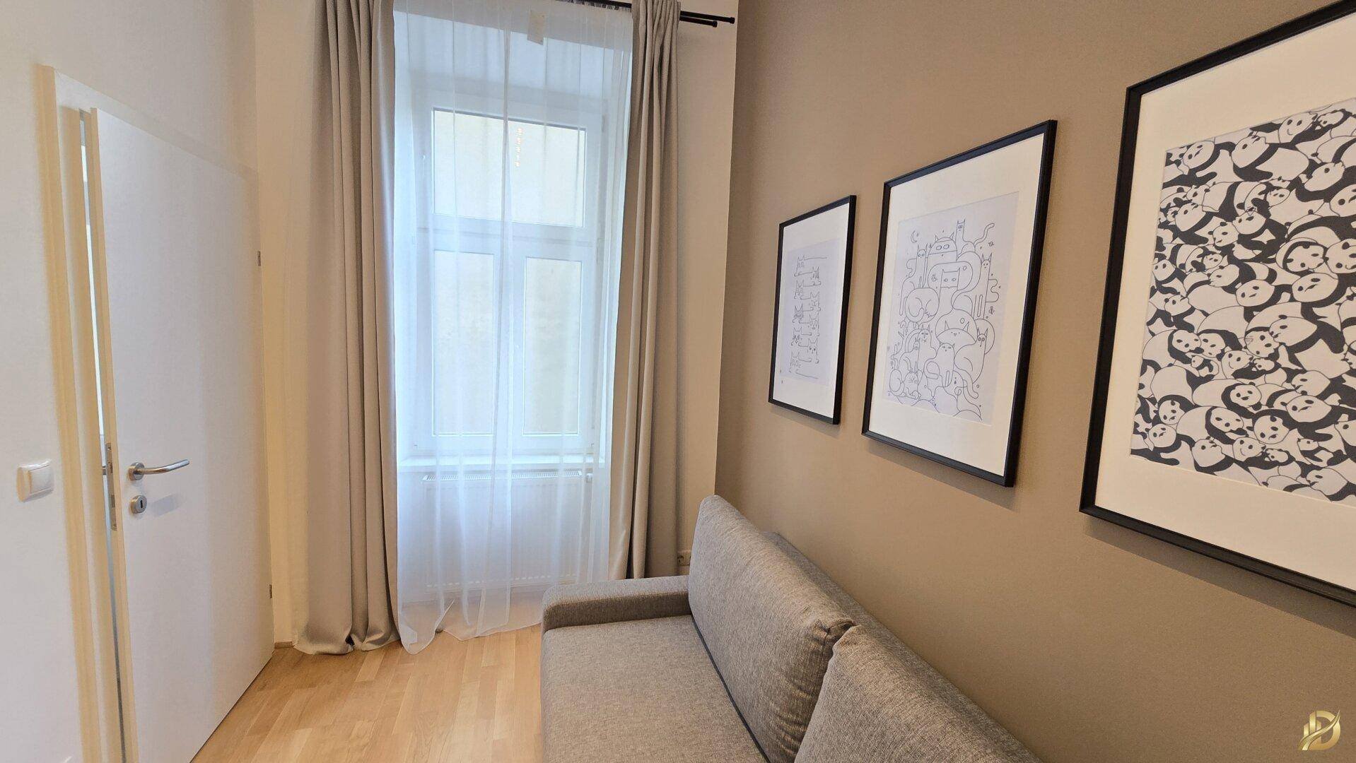 Heller Arbeitsbereich mit Fenster, Holzboden und Kunstwerken an der Wand.