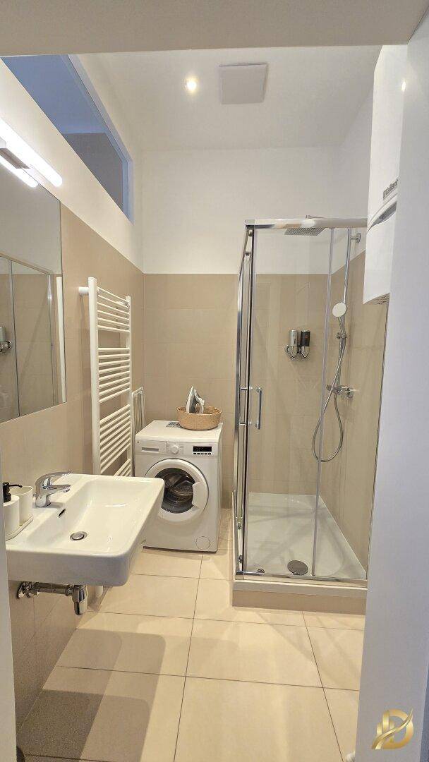 Modernes Badezimmer mit Duschkabine, Waschbecken, Handtuchheizkörper und Waschmaschine.