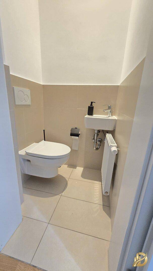 Separates WC mit wandhängender Toilette, kleinem Waschbecken und Heizkörper.