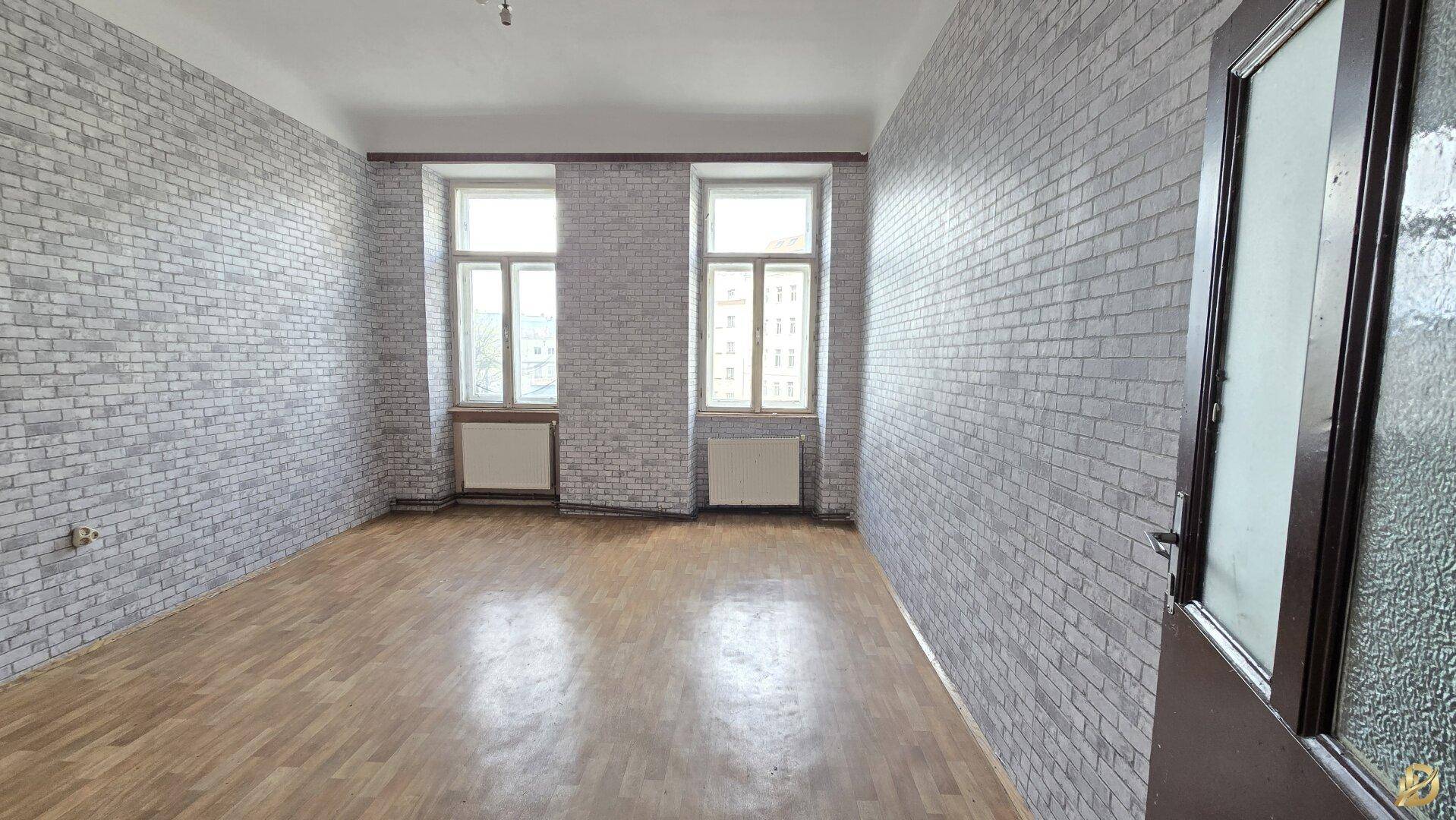 Helles Zimmer mit Laminatboden, Ziegelsteinoptik-Tapete und zwei Fenstern, ideal für eine Neugestaltung.