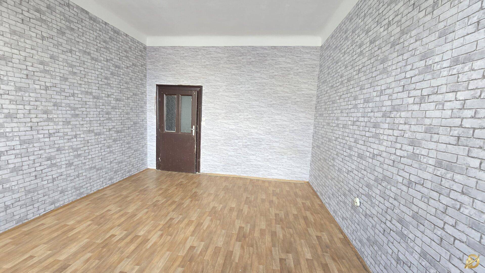 Leeres Zimmer mit Laminatboden und Tapete in Ziegelsteinoptik, bereit zur individuellen Gestaltung.