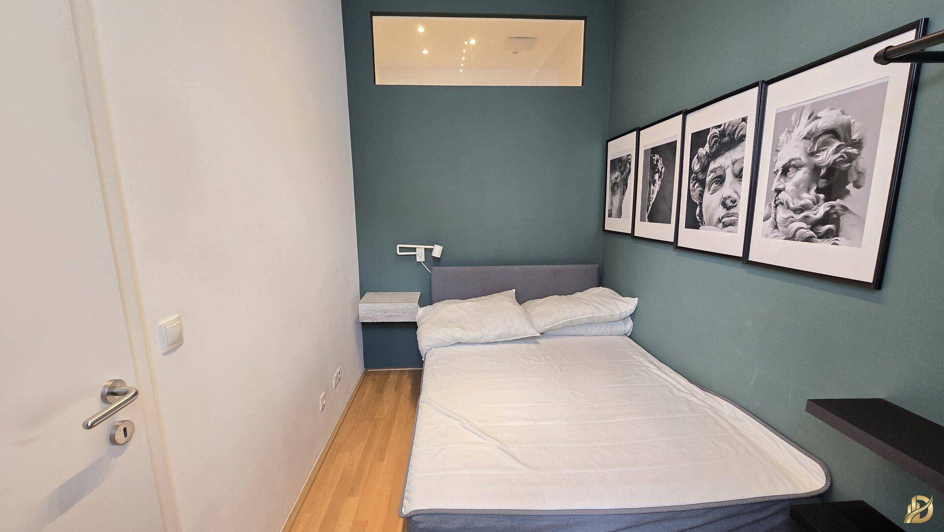 Modernes Schlafzimmer mit Doppelbett, dunkelgrüner Akzentwand und stilvollen Schwarz-Weiß-Bildern.