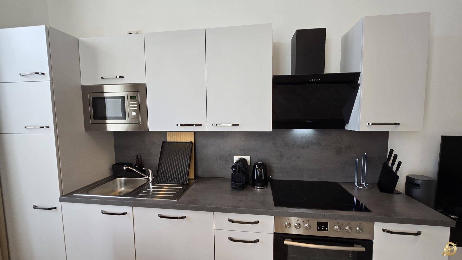 Moderne Küchenzeile mit weißen Schränken, integriertem Backofen, Mikrowelle und Induktionskochfeld.