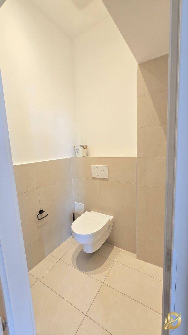 Separates WC mit wandhängender Toilette und hellen Fliesen an Wänden und Boden.
