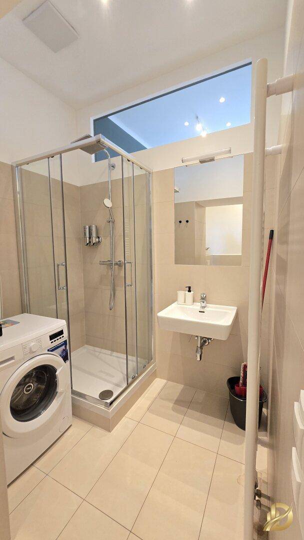 Modernes Badezimmer mit Duschkabine, Waschbecken und integrierter Waschmaschine.
