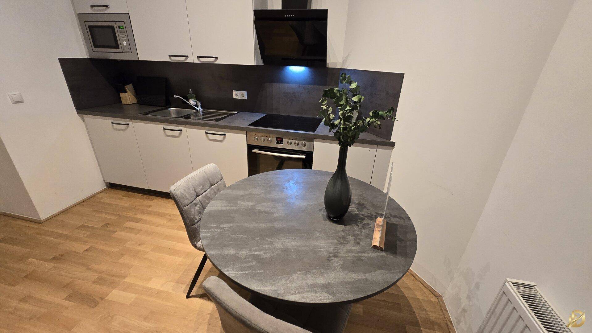 Küche mit Essbereich, dunkler Arbeitsplatte und modernen Geräten, gut beleuchtet.