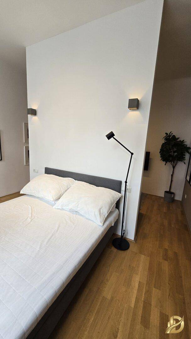 Schlafbereich mit Doppelbett und Stehlampe, durch eine Trennwand vom Wohnbereich abgetrennt.