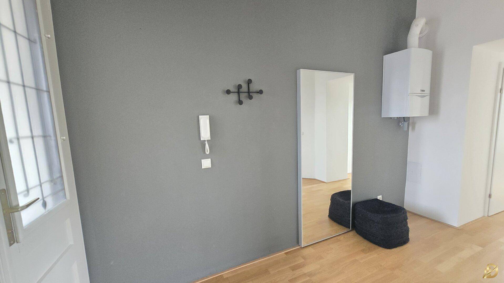 Flur mit grauer Wand, großem Spiegel und einer Heiztherme, die an der Wand montiert ist.