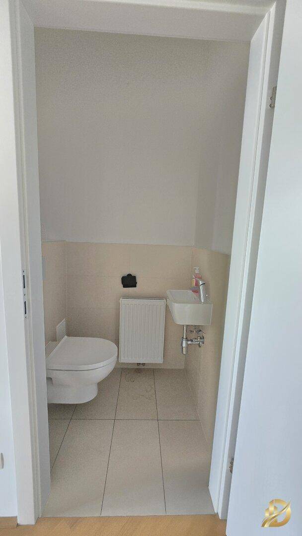 Kleines Gäste-WC mit Toilette, Handwaschbecken und Fliesenboden in hellem Farbton.