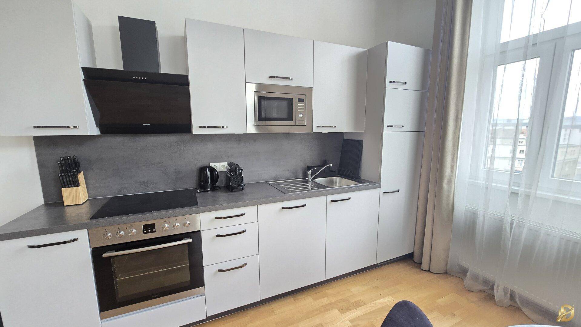 Moderne Einbauküche mit weißen Schränken, dunkler Arbeitsplatte und integrierten Elektrogeräten.