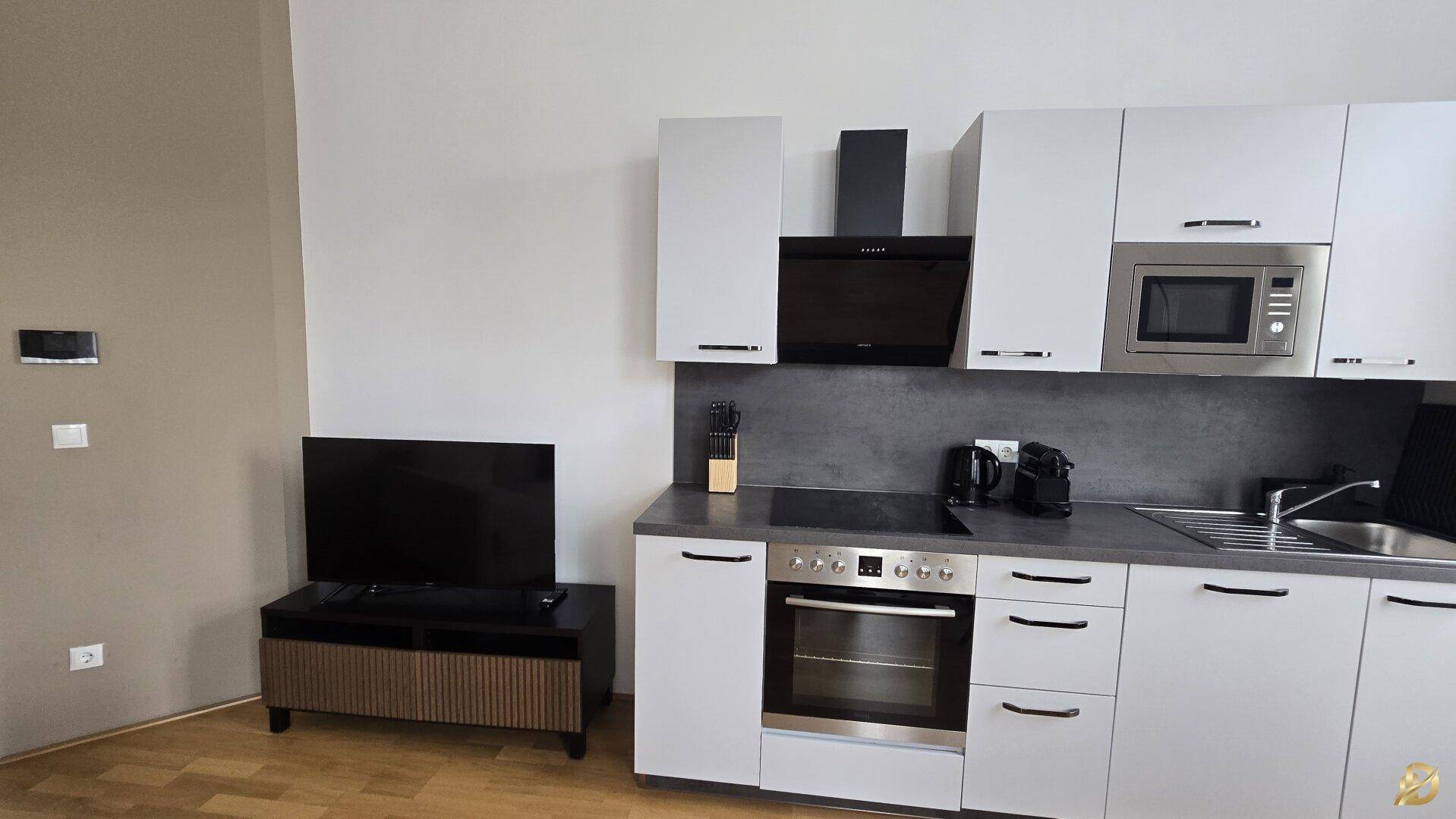 Detailansicht der modernen Küche mit weißen Fronten und einem Fernseher im angrenzenden Bereich.