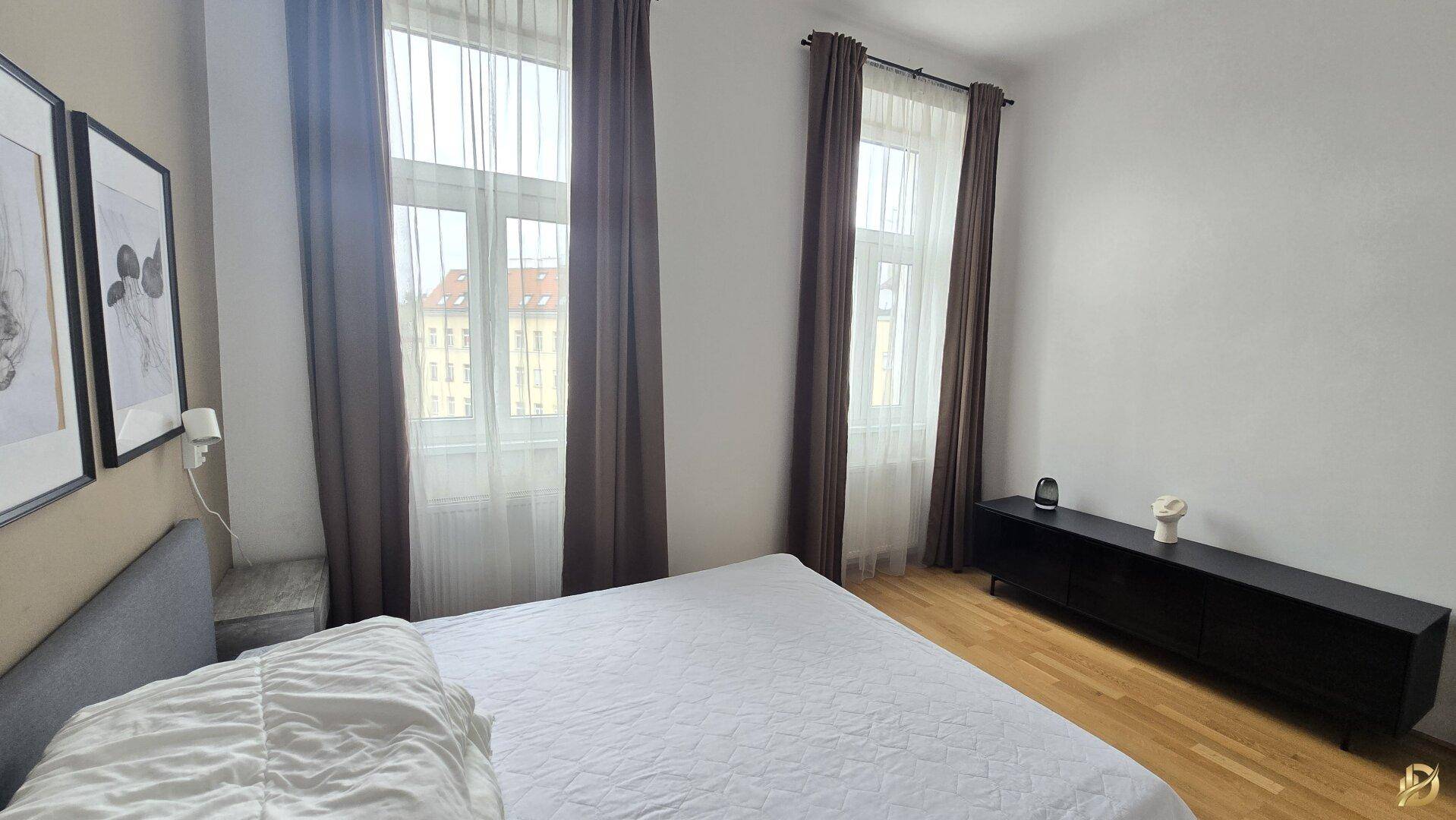 Geräumiges Schlafzimmer mit Doppelbett, Parkettboden und zwei hohen Fenstern für natürliche Belichtung.