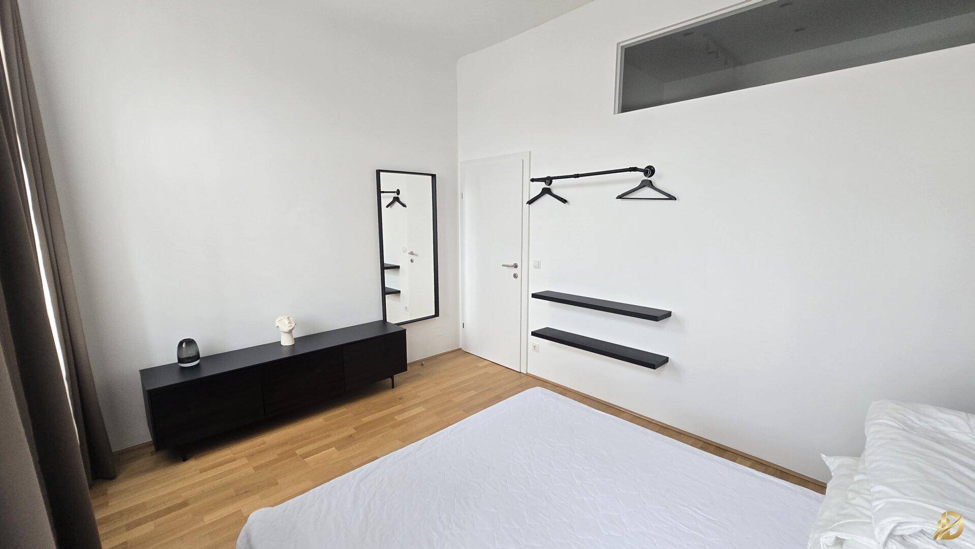 Schlafzimmer mit offener Garderobenlösung, Spiegel und einem Oberlicht für eine moderne Atmosphäre.