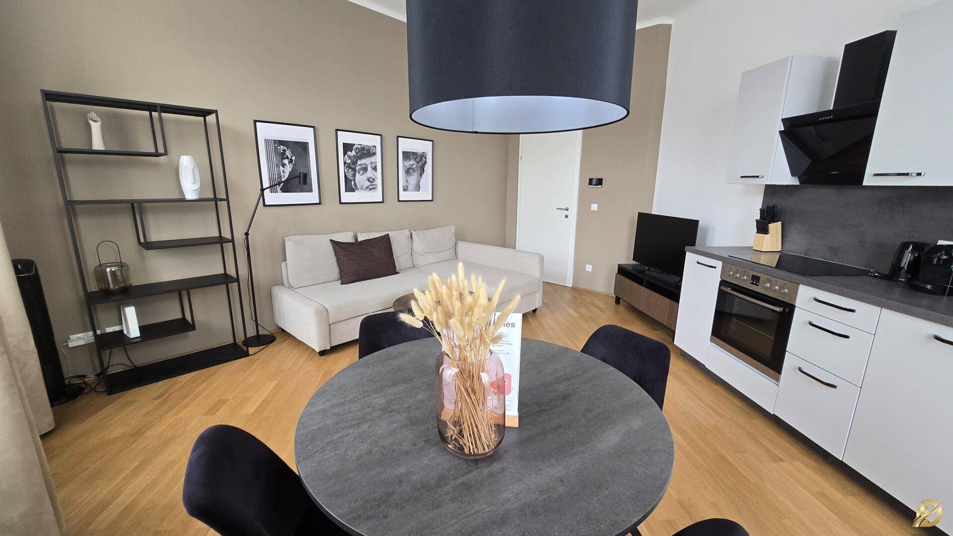 Essbereich mit runden Tisch und Blick auf die moderne Einbauküche und den Wohnbereich mit Sofa.