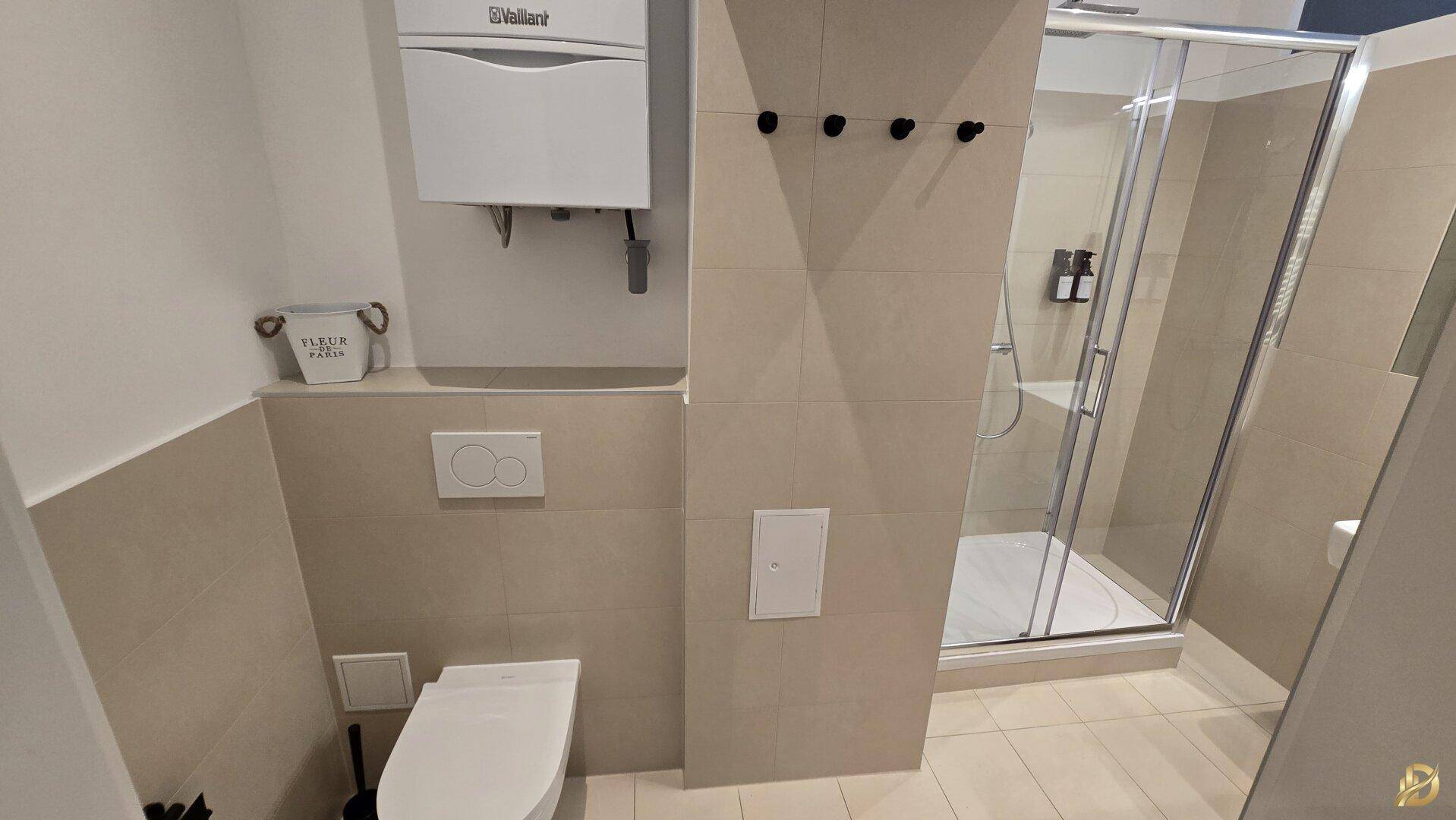 Modernes Badezimmer mit Duschkabine, wandhängendem WC und beigen Fliesen.