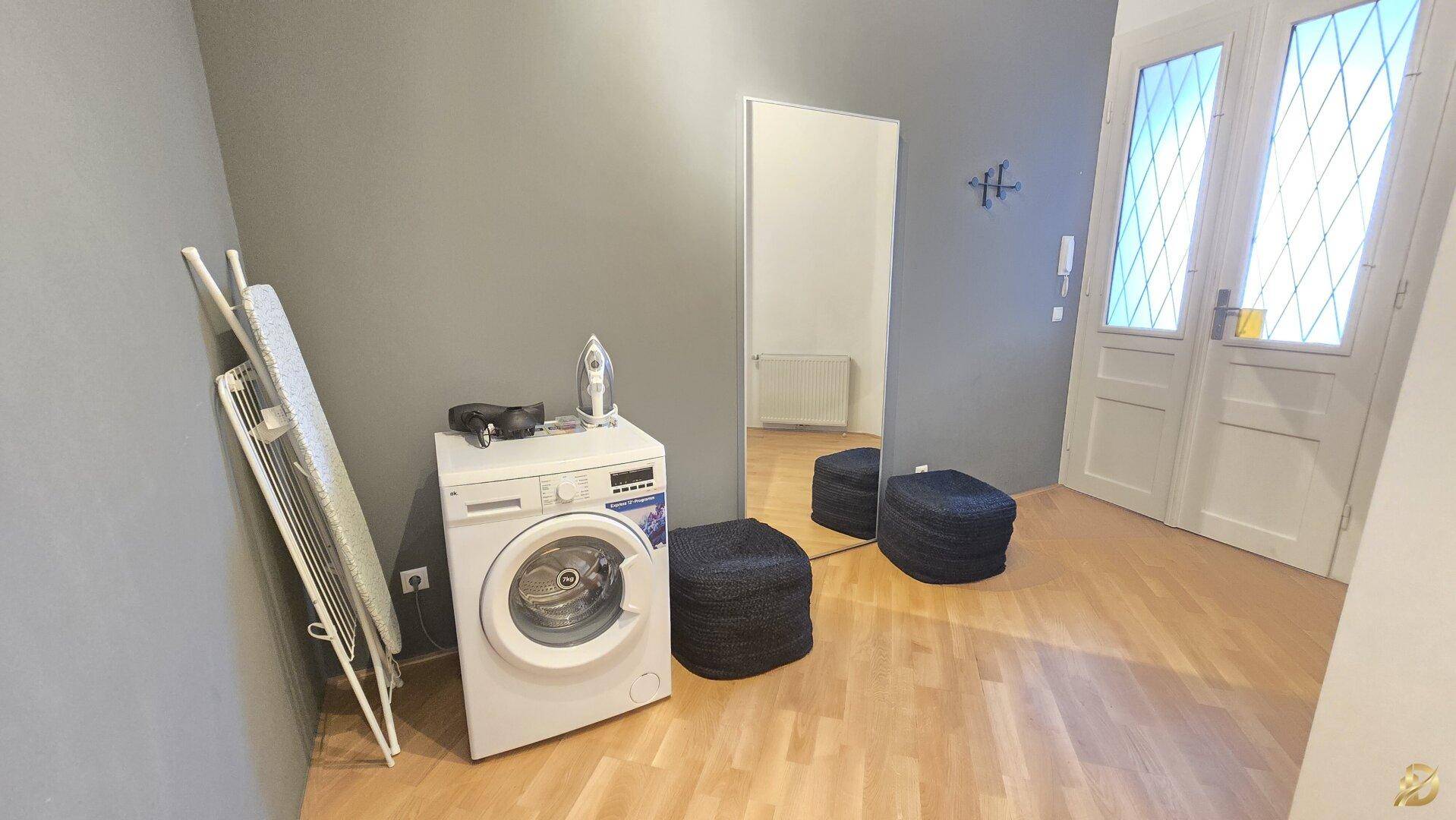 Hauswirtschaftsraum mit Waschmaschine, Bügelbrett und großem Spiegel.