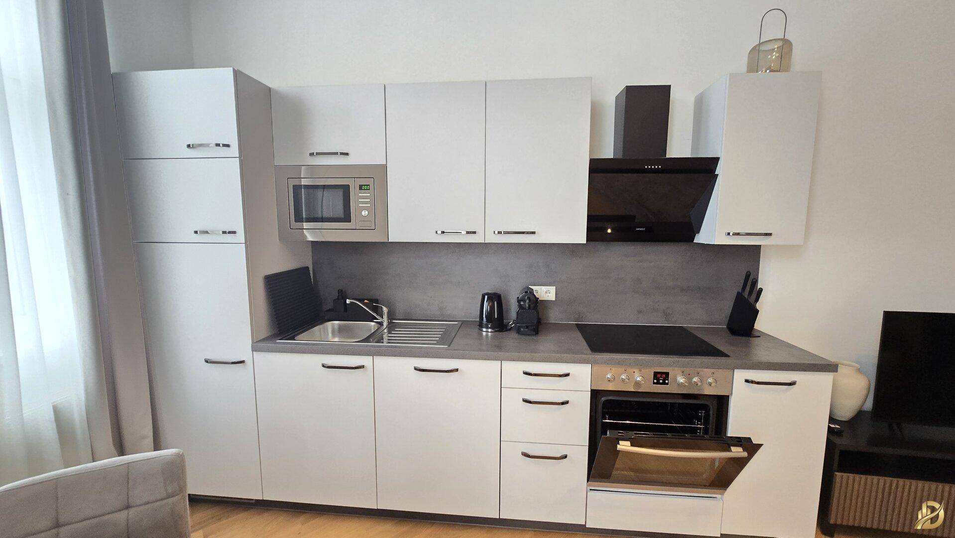 Moderne Küchenzeile mit weißen Schränken, integriertem Backofen und Mikrowelle.