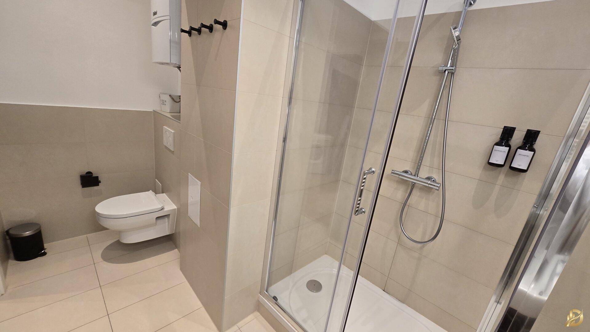 Helles Badezimmer mit Duschkabine, WC und beigefarbenen Wand- und Bodenfliesen.