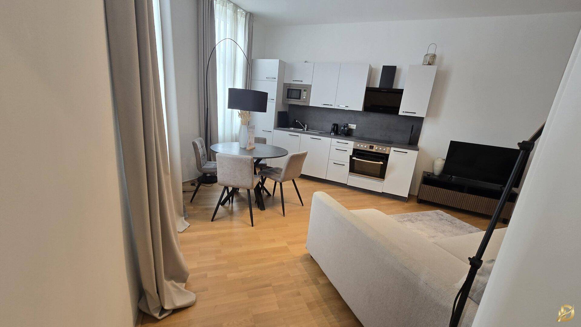 Heller Wohn-Essbereich mit moderner Küchenzeile, Esstisch und Sofa.