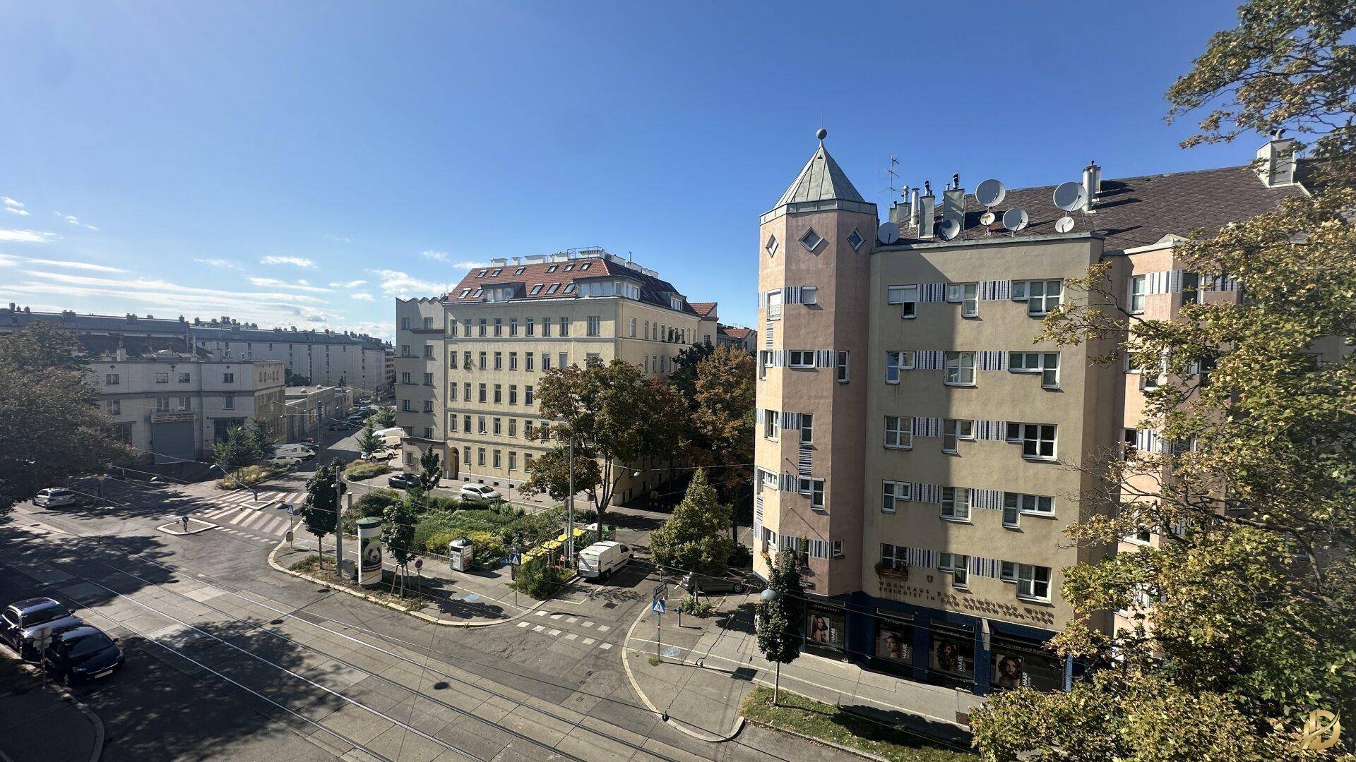 Weitläufiger Blick über eine Stadtstraße mit umliegenden Gebäuden und Bäumen.