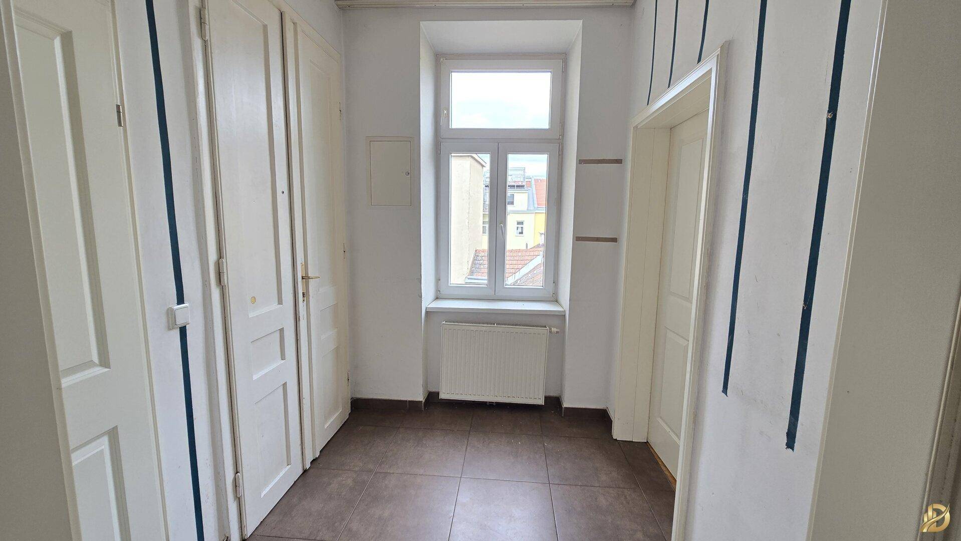 Flur mit dunklen Fliesen, einem Fenster und praktischen Einbauschränken.