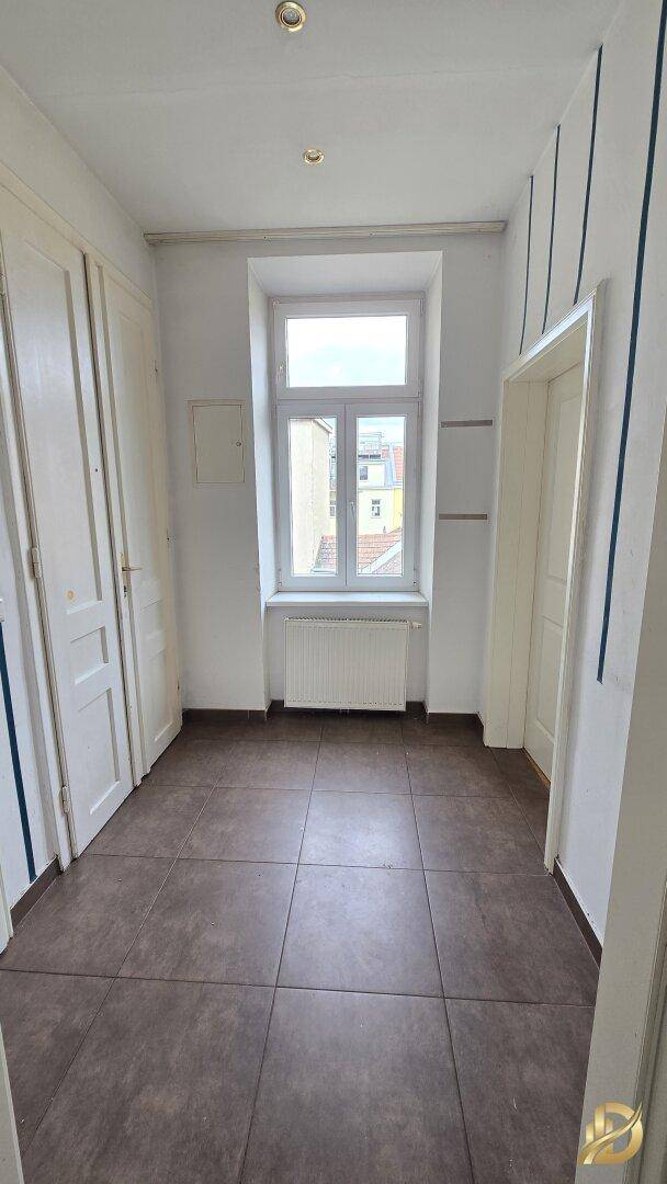 Eingangsbereich mit dunklen Fliesen und einem Fenster, das den Raum erhellt.