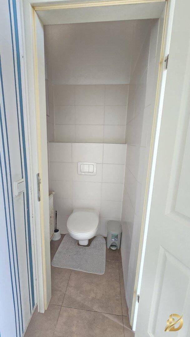 Separates WC mit wandhängender Toilette und hellen Fliesen an den Wänden.