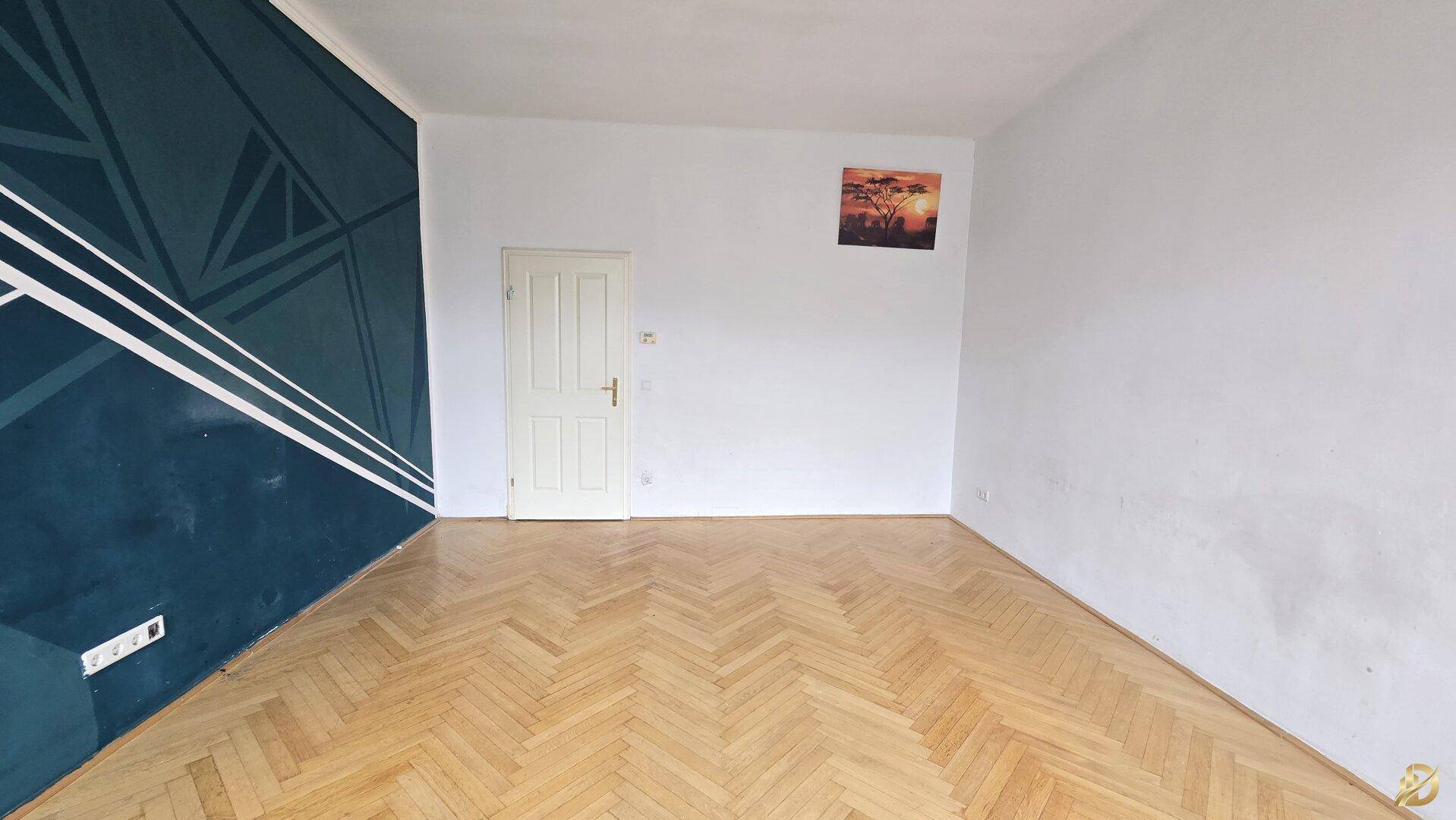 Heller Raum mit Fischgrätparkett und einer Tür, die zu weiteren Bereichen der Wohnung führt.