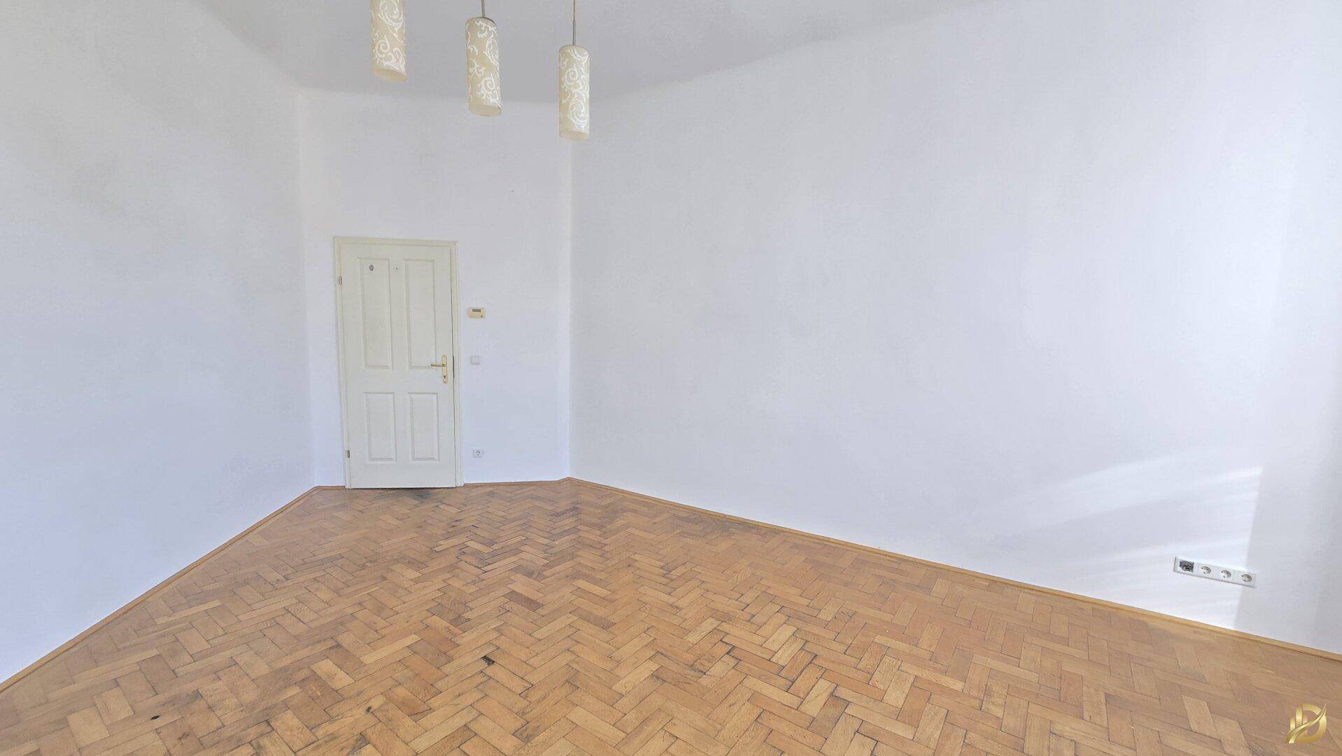 Geräumiges Zimmer mit Fischgrätparkett und einer Tür, die den Zugang ermöglicht.
