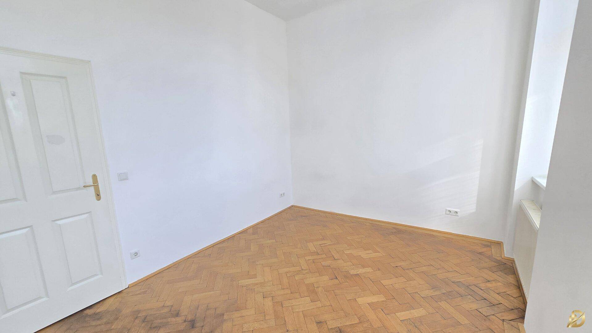 Helles Zimmer mit Parkettboden und einer Tür, die den Raum gut erschließt.