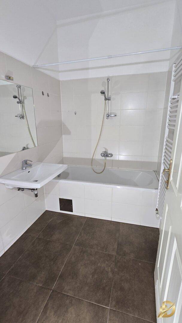 Badezimmer mit Badewanne, Waschbecken und Fliesen an Wänden und Boden.
