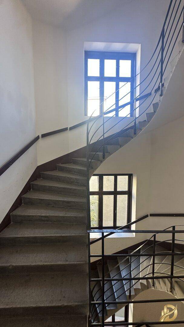 Geschwungenes Treppenhaus mit Metallgeländer und großen Fenstern, die den Bereich erhellen.