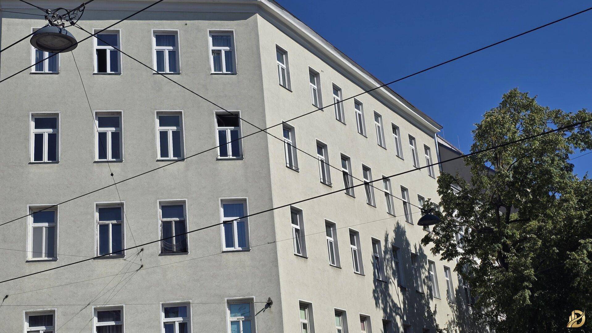 Fassade eines Mehrfamilienhauses mit vielen Fenstern unter blauem Himmel.