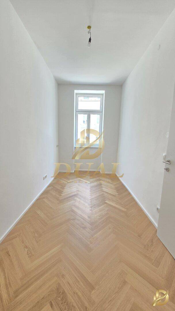Langer, heller Raum mit Fischgrätparkett und einem Fenster, das für natürliche Belichtung sorgt.