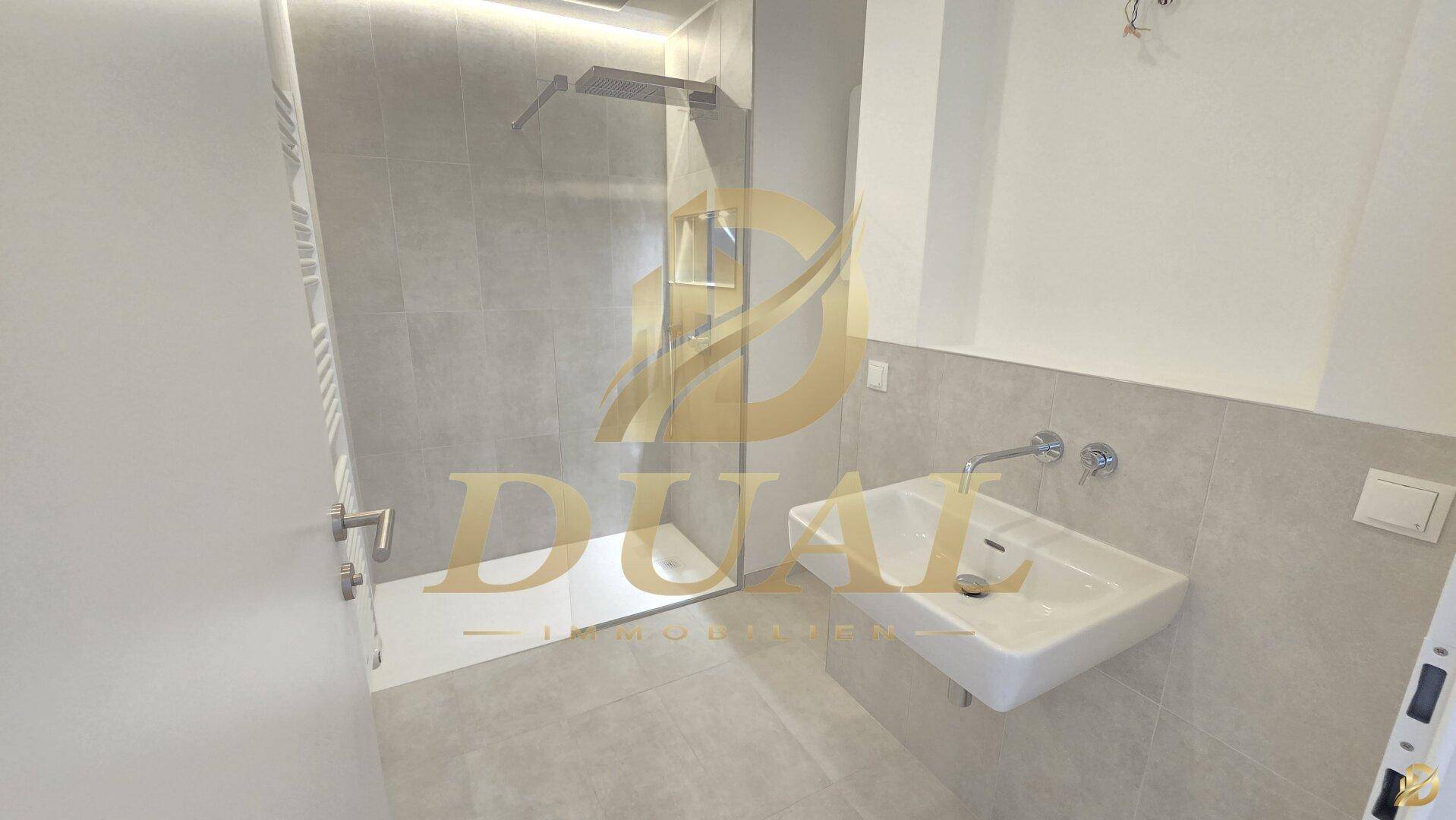 Modernes Badezimmer mit grauen Fliesen, ebenerdiger Dusche und einem einzelnen Waschbecken.