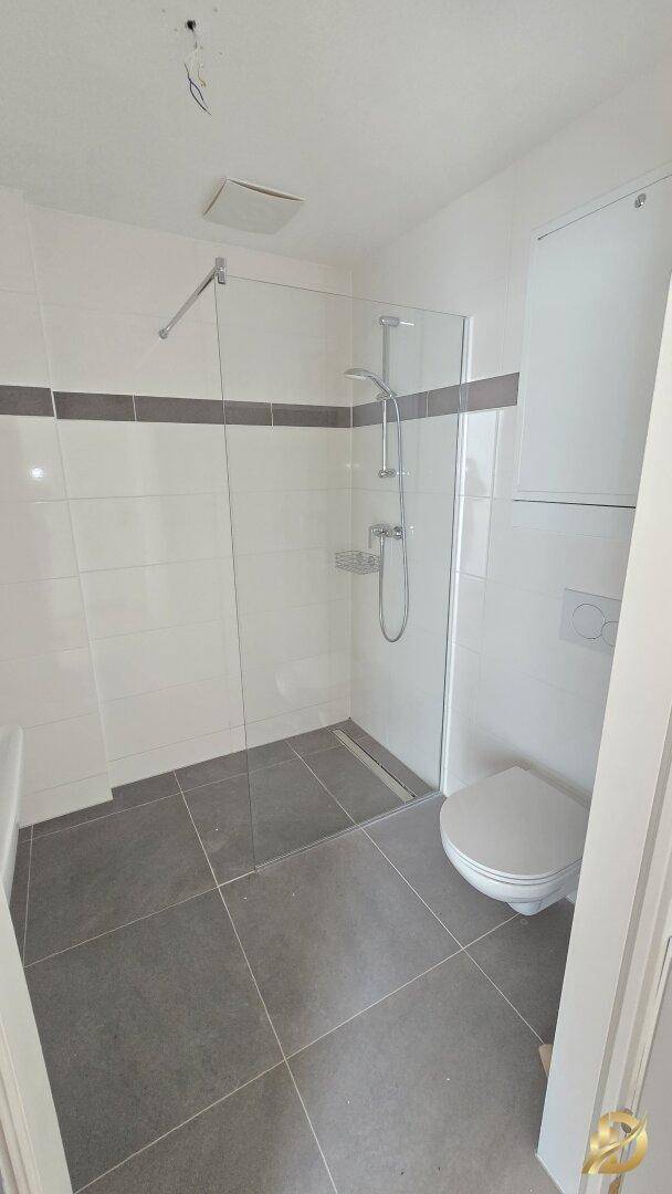 Modernes Badezimmer mit ebenerdiger Dusche, Wand-WC und grauen Fliesen.