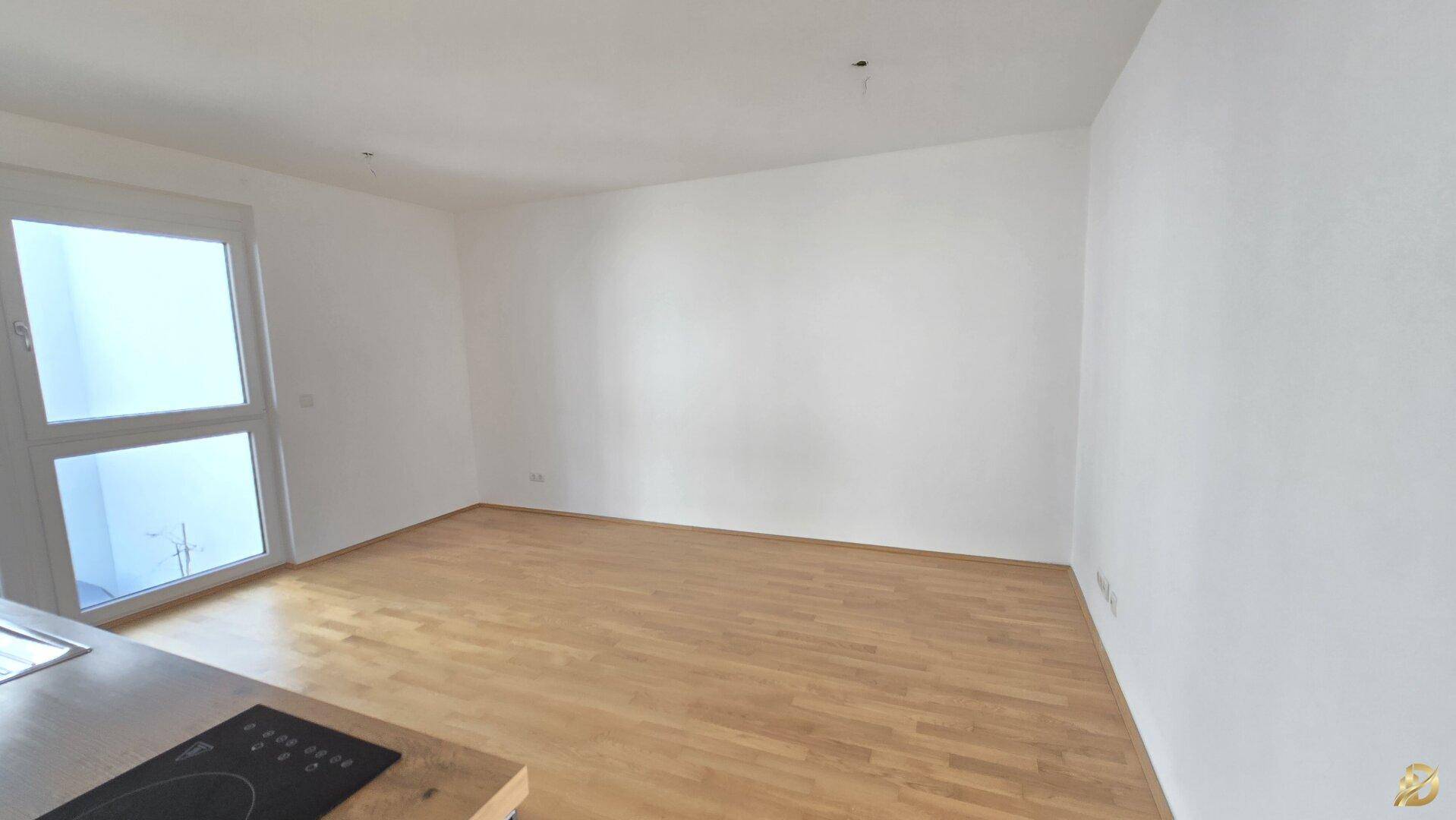 Heller Wohnbereich mit Parkettboden und großem Fenster, bereit zur Einrichtung.