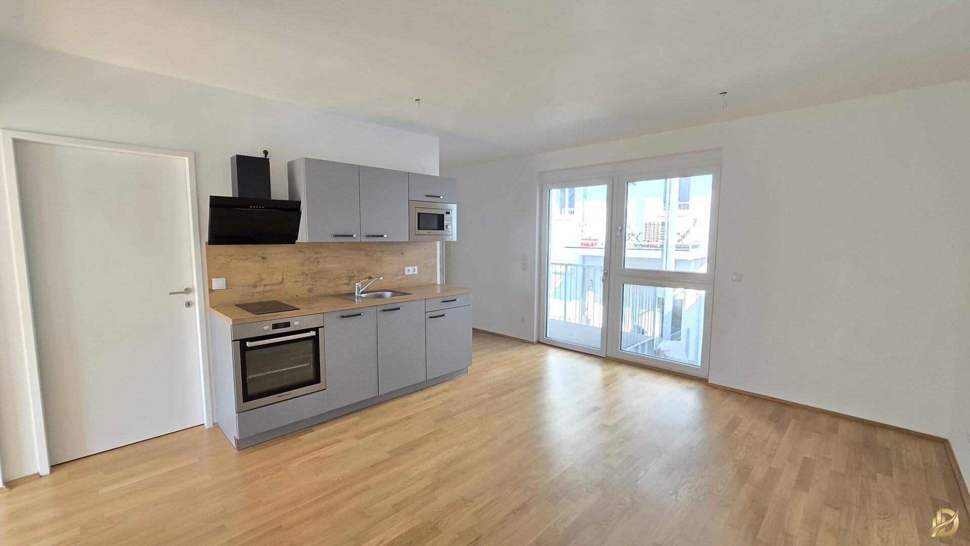 Heller offener Wohnbereich mit integrierter Küchenzeile und Zugang zum Balkon.