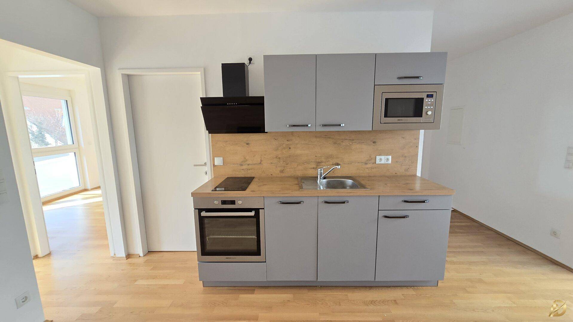 Moderne Küchenzeile mit grauen Schränken, Holz-Arbeitsplatte und Einbaugeräten.