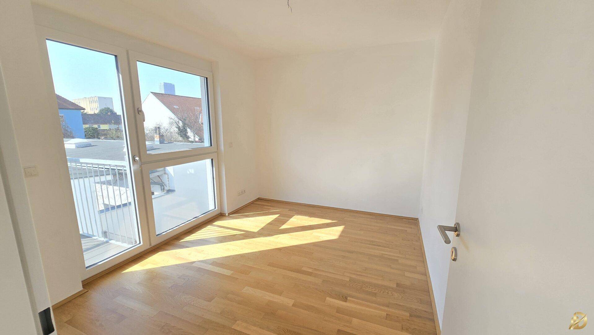Helles Schlafzimmer mit Holzboden und großem Fenster mit Zugang zum Balkon.