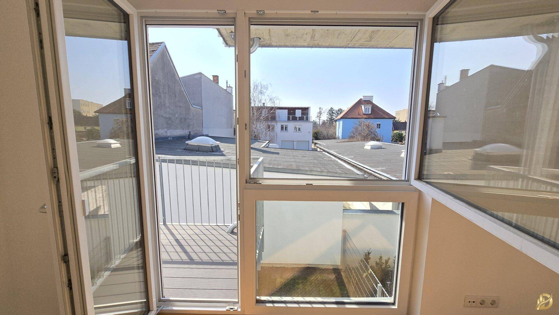 Blick aus dem Fenster auf die umliegenden Dächer und den blauen Himmel.