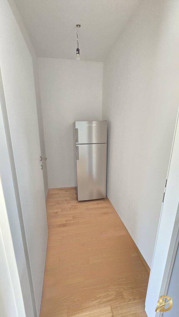 Kleiner Abstellraum mit einem Kühlschrank und hellem Holzboden.