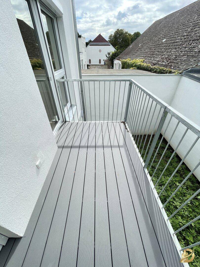 Heller Balkon mit modernem Bodenbelag und Blick auf eine Kirche in der Ferne.