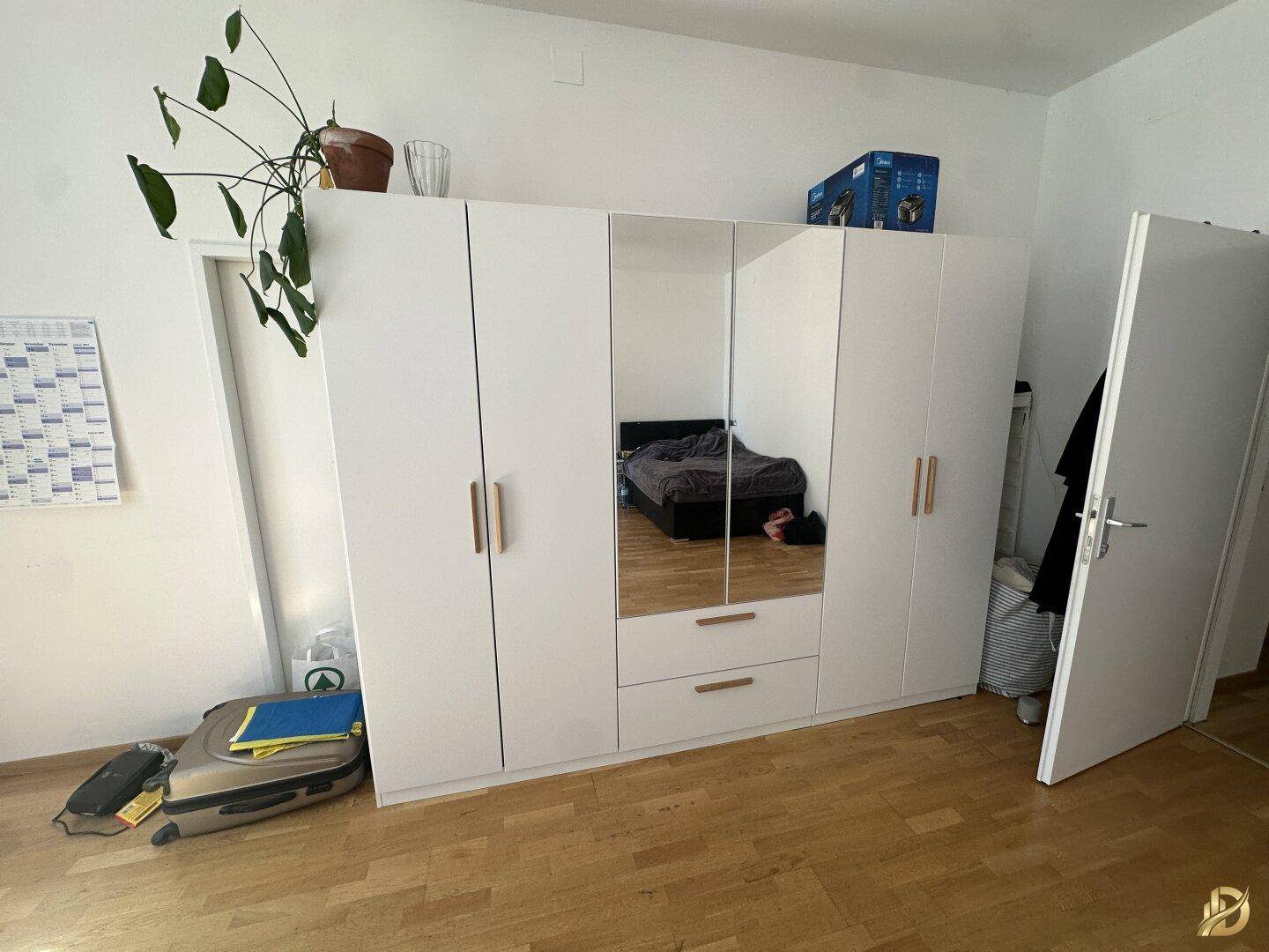Großer weißer Kleiderschrank mit Spiegeltüren in einem hellen Schlafzimmer.