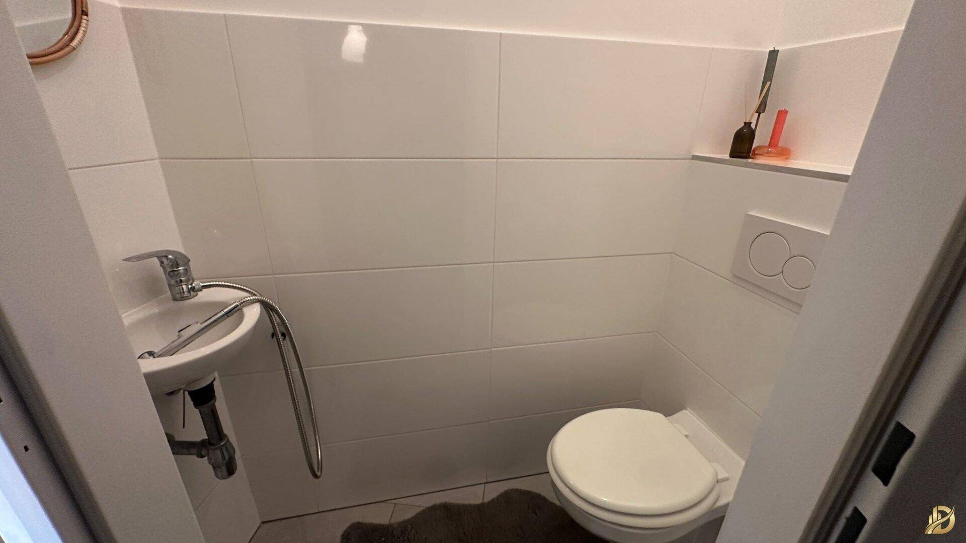 Kleines Gäste-WC mit Waschbecken und Toilette in weiß gefliestem Raum.