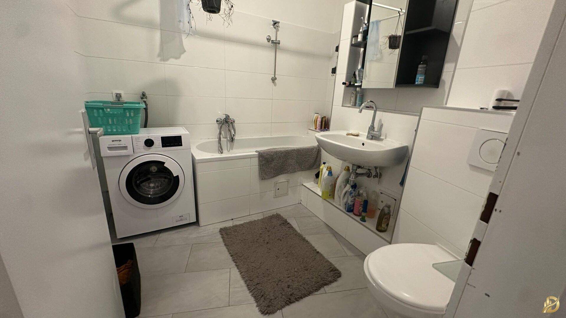 Helles Badezimmer mit Badewanne, Waschmaschine, Waschbecken und WC.