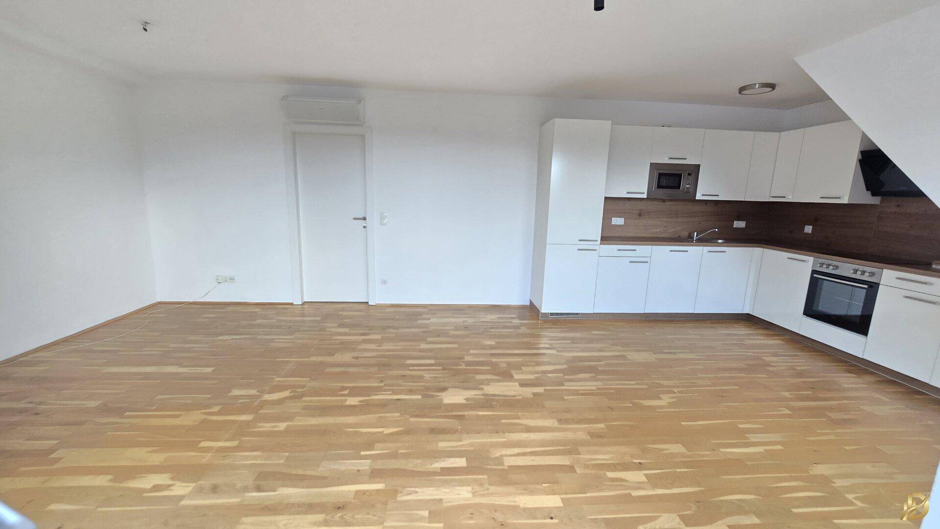 Offener Wohnbereich mit integrierter Küche und hellem Holzboden, ideal für geselliges Beisammensein.